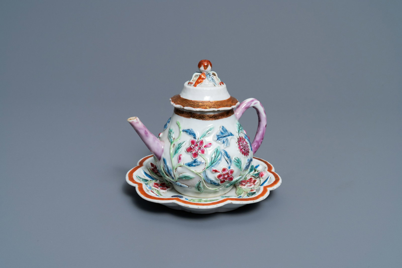 A Chinese famille rose relief-decorated teapot on: Full title: A Chinese famille rose relief-decorated teapot on stand, Yongzheng Description: Dia.: 16 cm (the stand) L.: 16 cm - H.: 13 cm (the teapot) The absence of a condition report does not imply