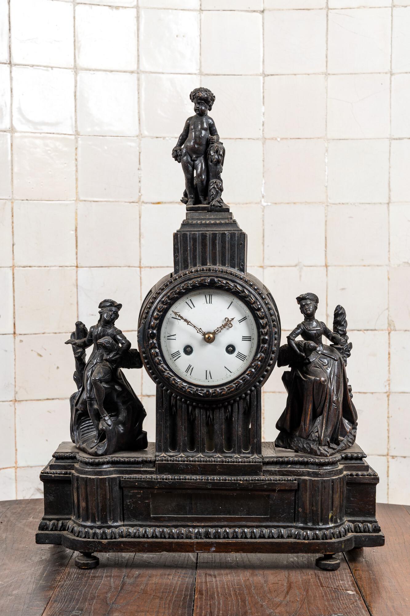 An ebonised mantel clock with romantic figures and topped with a putto, 19th C. (1 of 4)