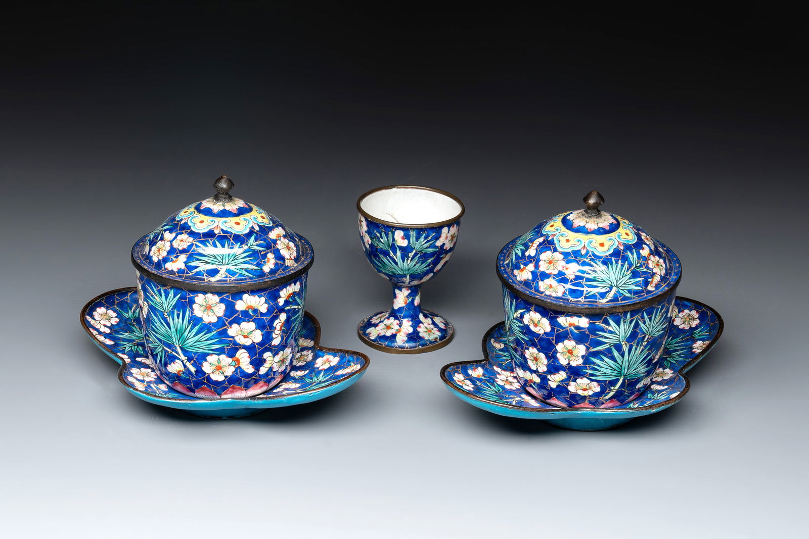 A pair of Chinese blue-ground Canton enamel covered bowls on stands and an egg cup, Qianlong/Jiaqing: A pair of Chinese blue-ground Canton enamel covered bowls on stands and an egg cup, Qianlong/Jiaqing Dia.: 7,7 cm - H.: 10 cm (the bowls incl. cover) Dim.: 10,2 x 14,5 cm (the stands) Dia.: 4,8 cm - H