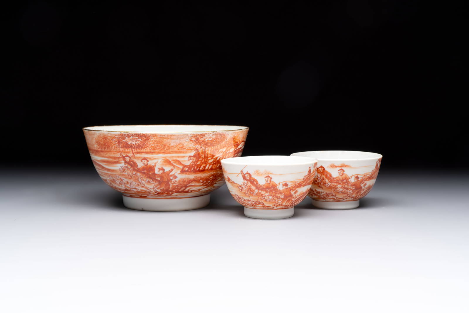 A Chinese iron-red-decorated 'Deer Hunting' bowl and two cups, Qianlong