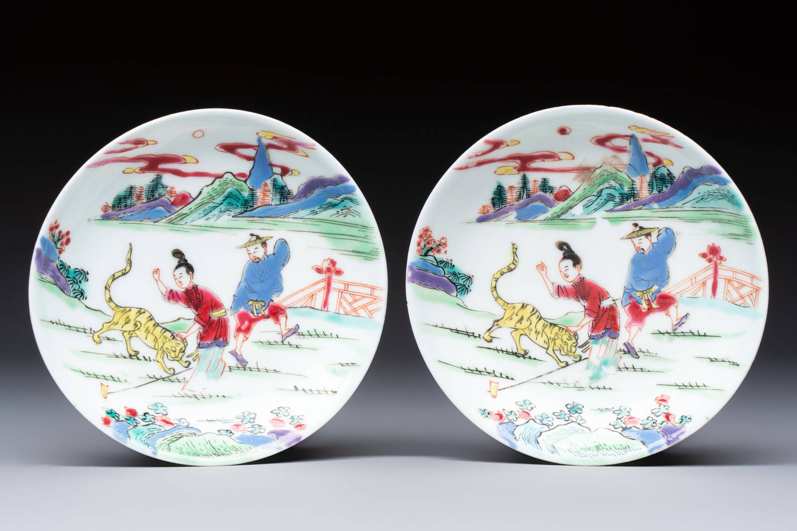 A pair of Chinese famille rose 'Taming the Tiger' saucers, Yongzheng