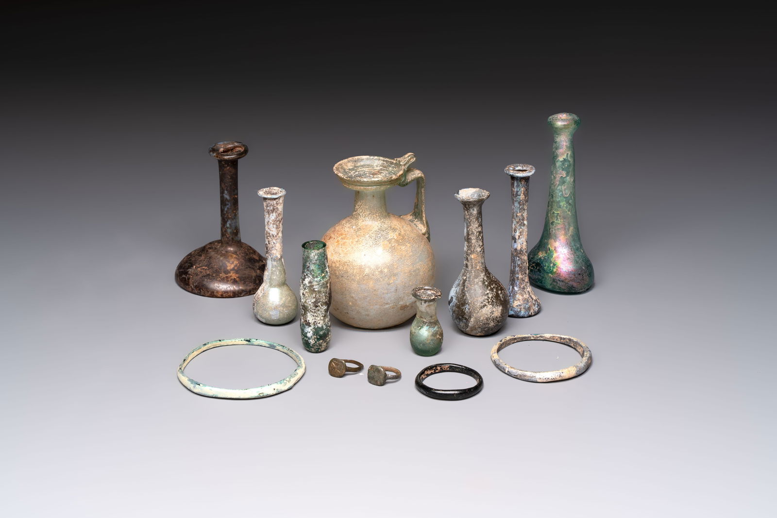 Eight Roman glass flasks, three glass bracelets and two bronze rings, 1st/4th C.: Eight Roman glass flasks, three glass bracelets and two bronze rings, 1st/4th C. H.: 12 cm (the tallest flask) H.: 4,2 cm (the smallest flask) Dia.: 8 cm (the largest bracelet) Dia.: 4,2 cm (the small