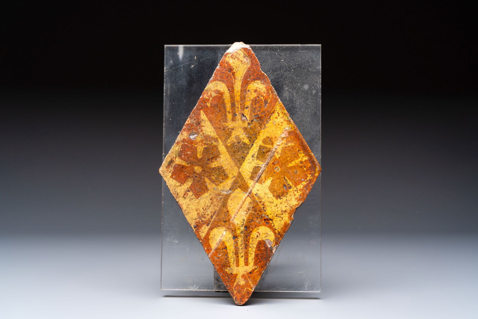 A medieval lozenge-shaped 'Fleur-de-Lys' tile, Chateau de Beaute, France, 14th C.: A medieval lozenge-shaped 'Fleur-de-Lys' tile, Chateau de Beaute, France, 14th C. Dim.: 21,6 x 13,4 x 2,7 cm (excl. mount)