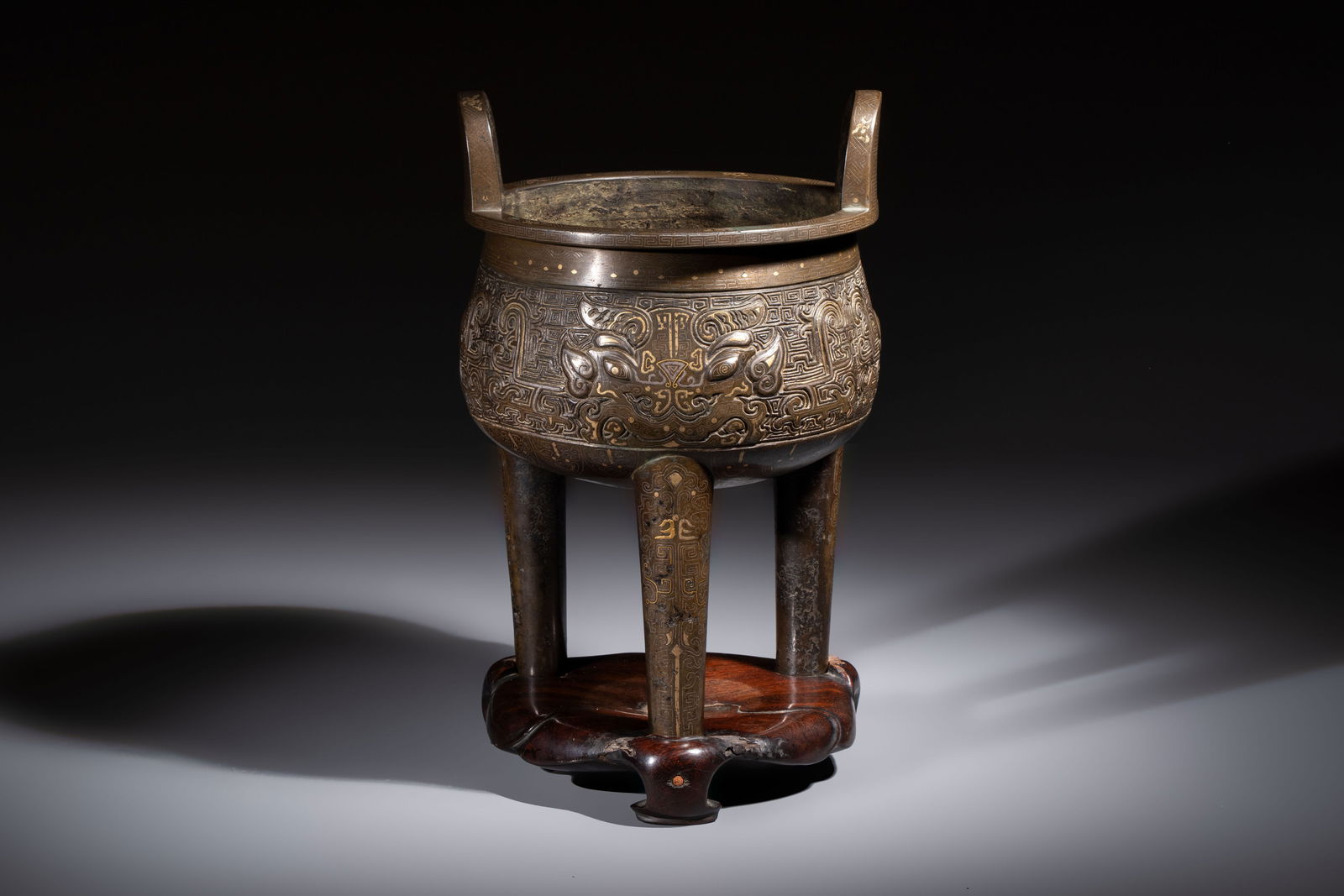 A rare Chinese gold- and silver-inlaid bronze 'Ding' censer with Taotie design on a hongmu stand, (1 of 8)