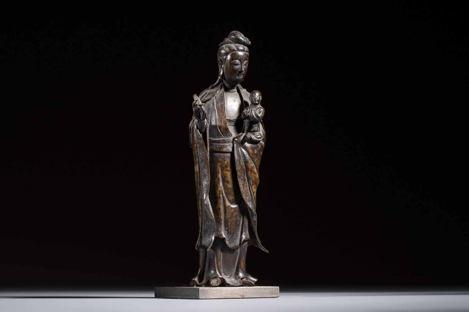 A Chinese bronze standing Guanyin with boy, Ming: A Chinese bronze standing Guanyin with boy, Ming H.: 20,7 cm (incl. stand) H.: 19,7 cm (excl. stand) Weight: 880 grams (incl. stand)