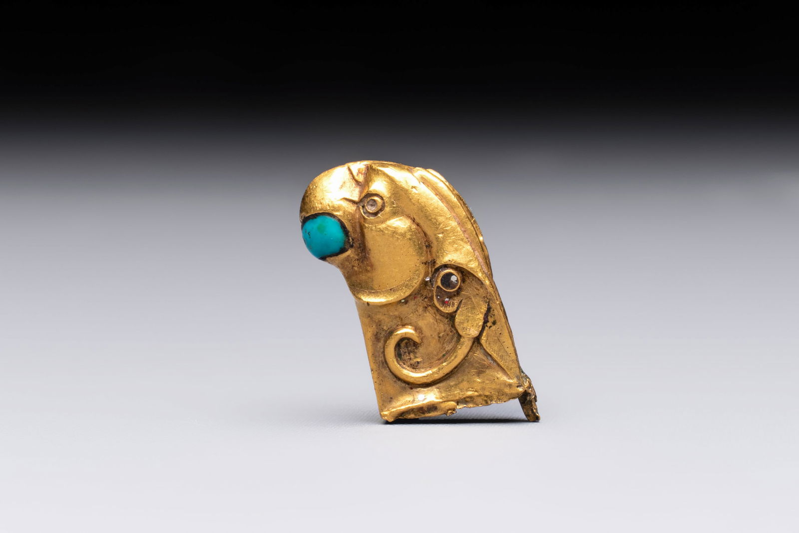 A rare Chinese turquoise- and glass-inlaid gold fitting in the form of a parrot, Han: A rare Chinese turquoise- and glass-inlaid gold fitting in the form of a parrot, Han Dim.: 2,2 x 1,3 cm Weight: 6,97 grams (total) Ref.: Sotheby's, New York, Sept. 22, 2021, lot 43, for a comparable g