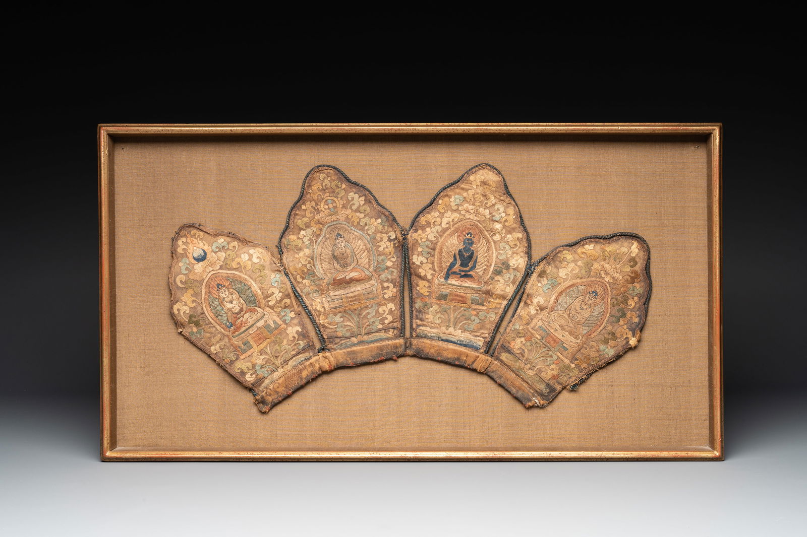 A framed Tibetan silk-embroidered four-leaf ritual crown with Transcendent Buddhas, 18th C.: A framed Tibetan silk-embroidered four-leaf ritual crown with Transcendent Buddhas, 18th C. Dim.: 23 x 85 cm (the frame) Dim.: 20,5 x 48,5 cm (the crown) Provenance: - From the collection of Mr. and M
