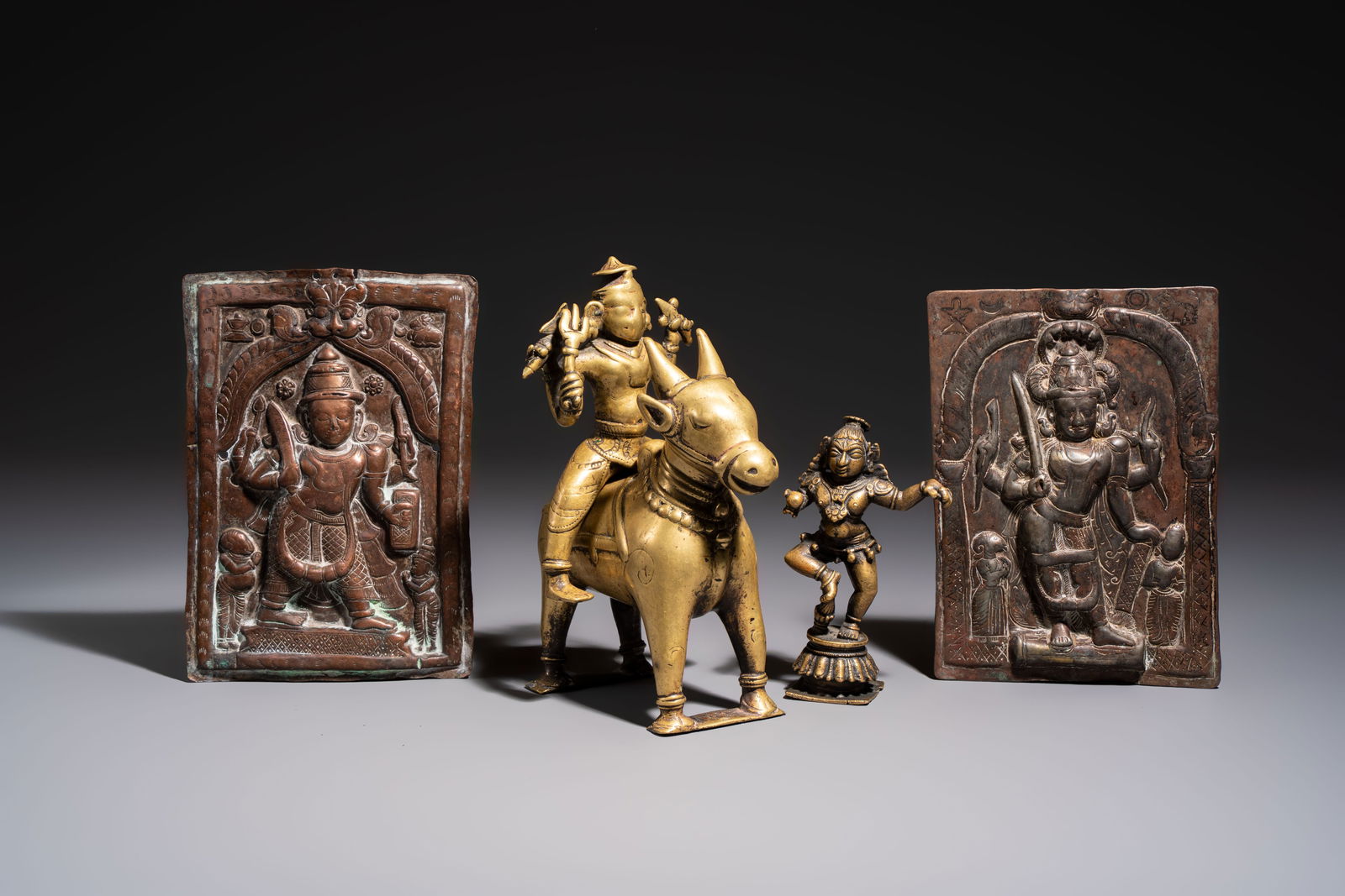 Two Indian bronze figures and two repoussé copper-alloy plaques, 18/19th C.: Two Indian bronze figures and two repoussé copper-alloy plaques, 18/19th C. H.: 21 cm (the rider on a bull) H.: 14 cm (the statue) Dim.: 21,5 x 15 cm (the plaques) Weight: - 2075 grams (the rider on
