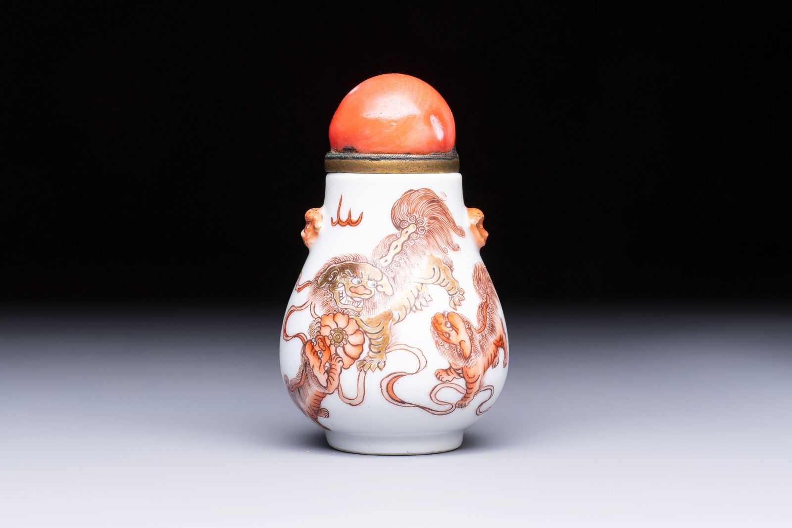 A Chinese gilt-decorated iron-red 'Buddhist Lions' snuff bottle with a red coral stopper, Buddhist (1 of 7)