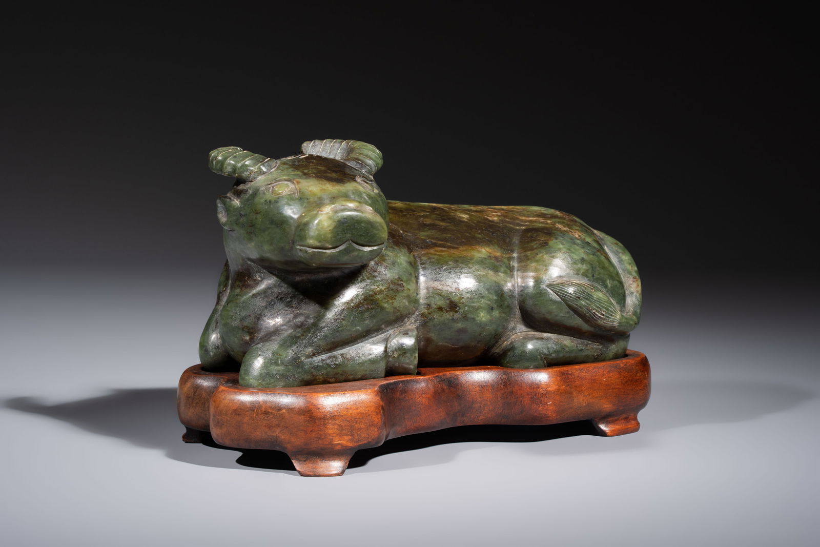 A Chinese green jade reclining buffalo on a wooden stand, 19/20th C. (1 of 7)