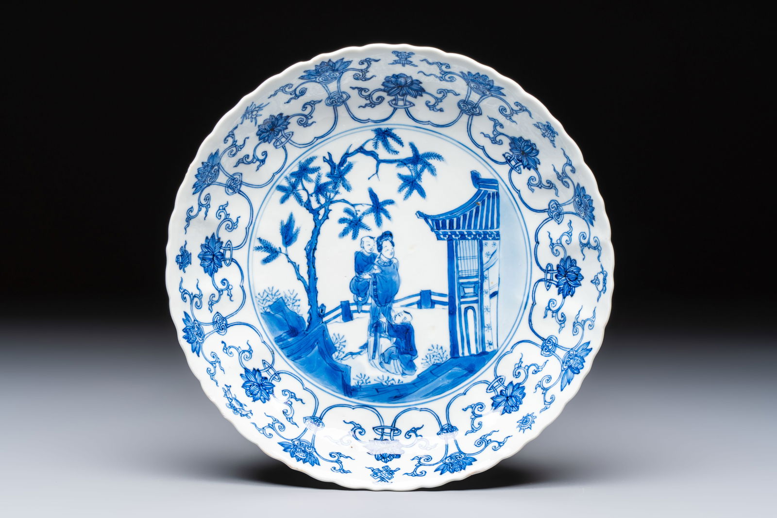 A Chinese blue and white 'Elegant Lady with Two Boys' plate with a 'Lotus Scroll' border, Kangxi (1 of 2)