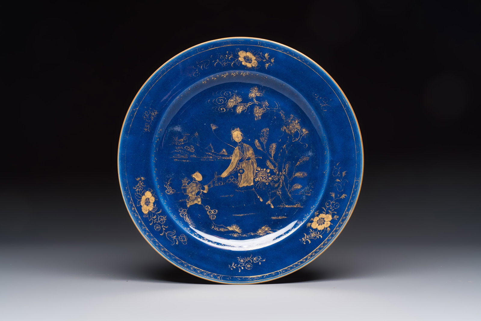 A Chinese gilt-decorated powder-blue-ground 'Elegant Beauty and Boy' dish, Kangxi (1 of 2)