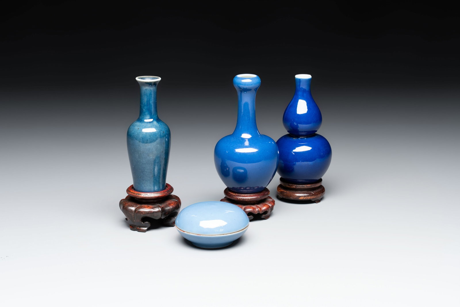 Three Chinese blue-glazed miniature vases on wooden stands and a claire-de-lune seal paste box and: Three Chinese blue-glazed miniature vases on wooden stands and a claire-de-lune seal paste box and cover, 19th C. H.: 11,3 cm (the tallest vase, excl. stand) H.: 10,6 cm (the smallest vase, excl. stan