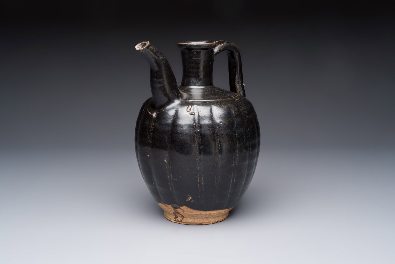 A Chinese Yaozhou black-glazed ewer with a ribbed body, Song: A Chinese Yaozhou black-glazed ewer with a ribbed body, Song L.:18,3 cm - H.: 24,8 cm Provenance: - A Belgian private collection,Antwerp.