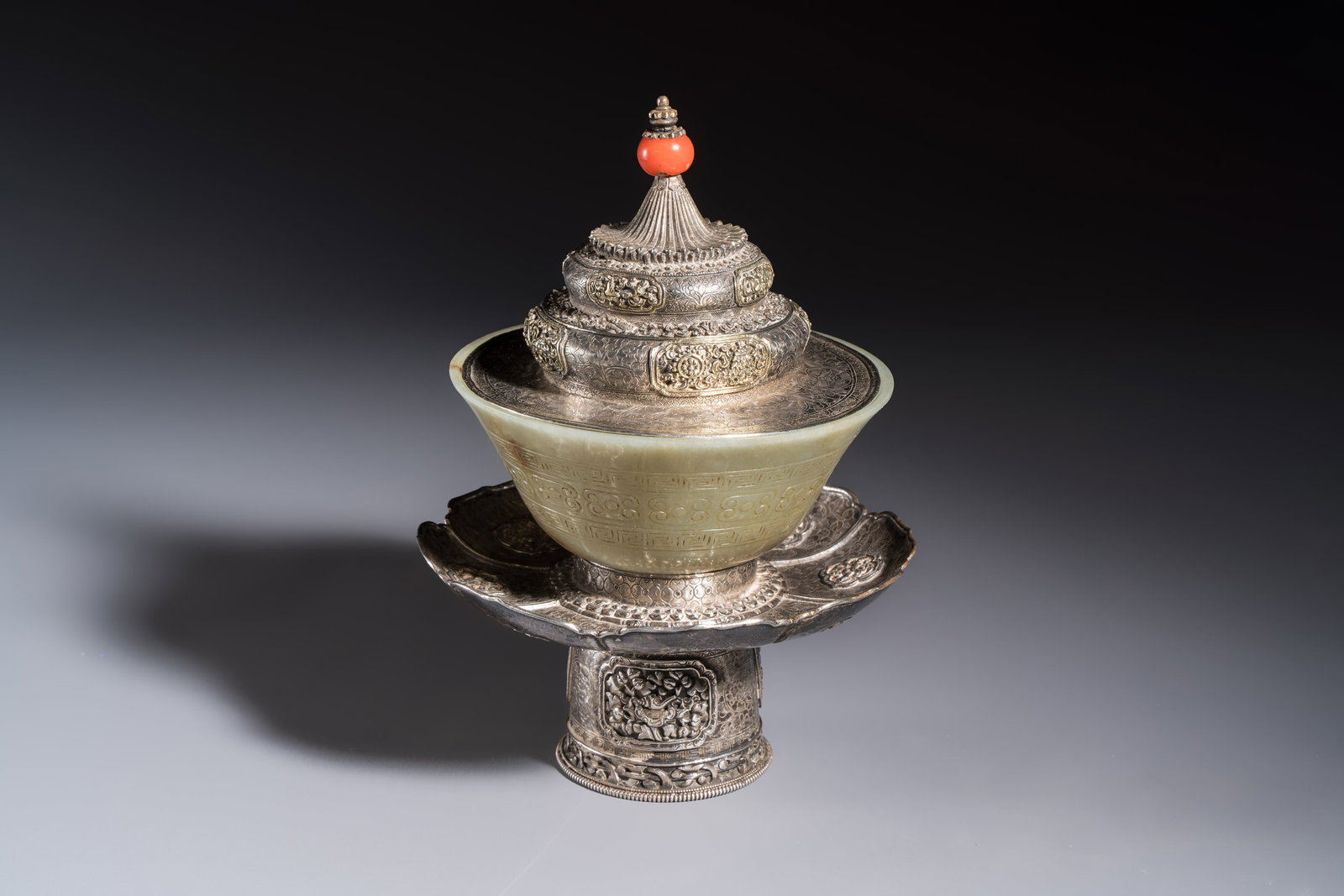 A Tibetan ritual jade bowl with a red coral-mounted silver cover and a stand, 19th C. (1 of 16)