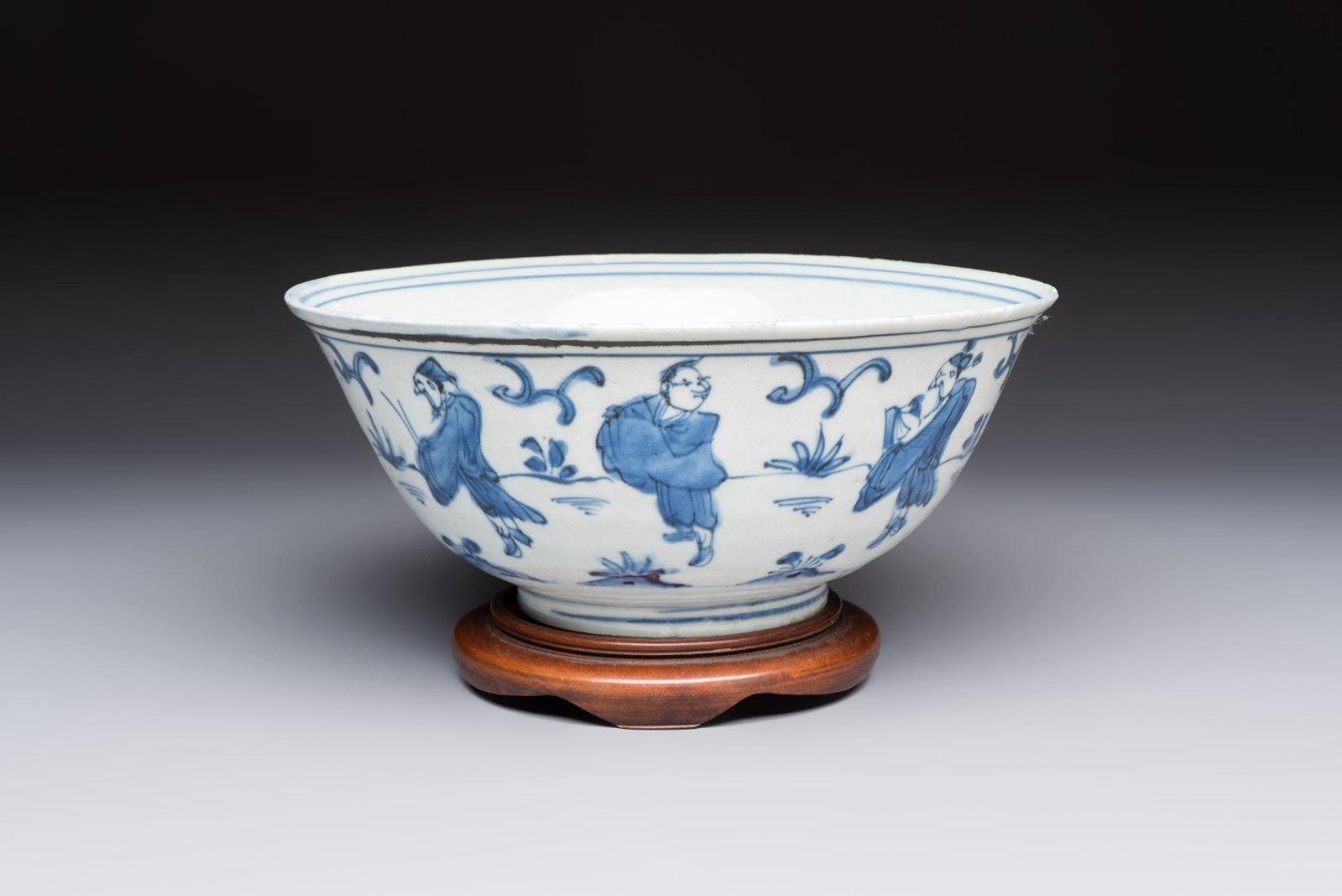 A Chinese blue and white 'Eight Immortals' bowl on a wooden stand, Chenghua mark, late Ming: A Chinese blue and white 'Eight Immortals' bowl on a wooden stand, Chenghua mark, late Ming Dia.: 22,5 cm - H.: 11,7 cm (incl. stand) Dia.: 22,5 cm - H.: 9,6 cm (excl. stand)