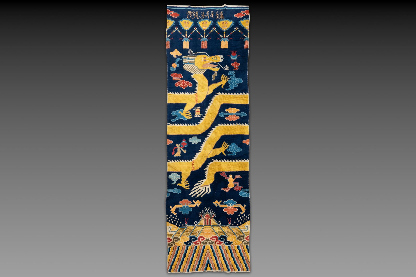 A Sino-Tibetan inscribed woollen 'Dragon' pillar carpet, 19th C.: A Sino-Tibetan inscribed woollen 'Dragon' pillar carpet, 19th C. Dim.: 473 x 141 cm Many Chinese Buddhist objects from the Qing Dynasty have links with Mongolia, as does this pillar carpet. This rug w