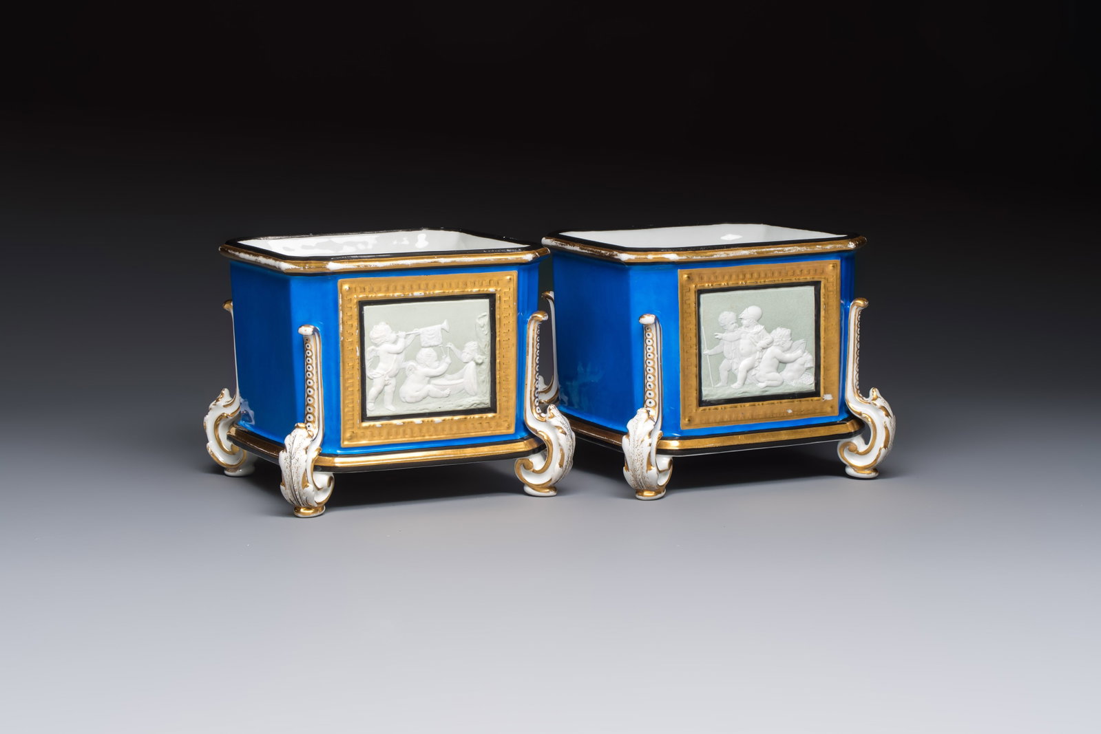 A pair of French gilt blue-ground 'Cherub' jardinières with biscuit-relief plaques, 19/20th C.: A pair of French gilt blue-ground 'Cherub' jardinières with biscuit-relief plaques, 19/20th C. Dim.: 17,7 x 17,7 x 14,9 cm