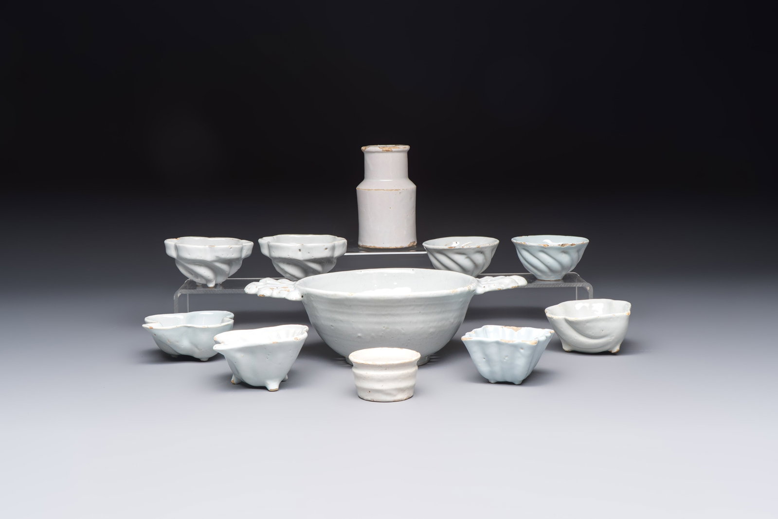 A collection of nine white-glazed Dutch Delft pudding moulds, a mustard pot and a two-handled: A collection of nine white-glazed Dutch Delft pudding moulds, a mustard pot and a two-handled strainer, 18th C. L.: 24,8 cm - H.: 7,1 cm (the strainer) H.: 10,5 cm (the mustard pot) Dia.: 8,6 cm - H.: