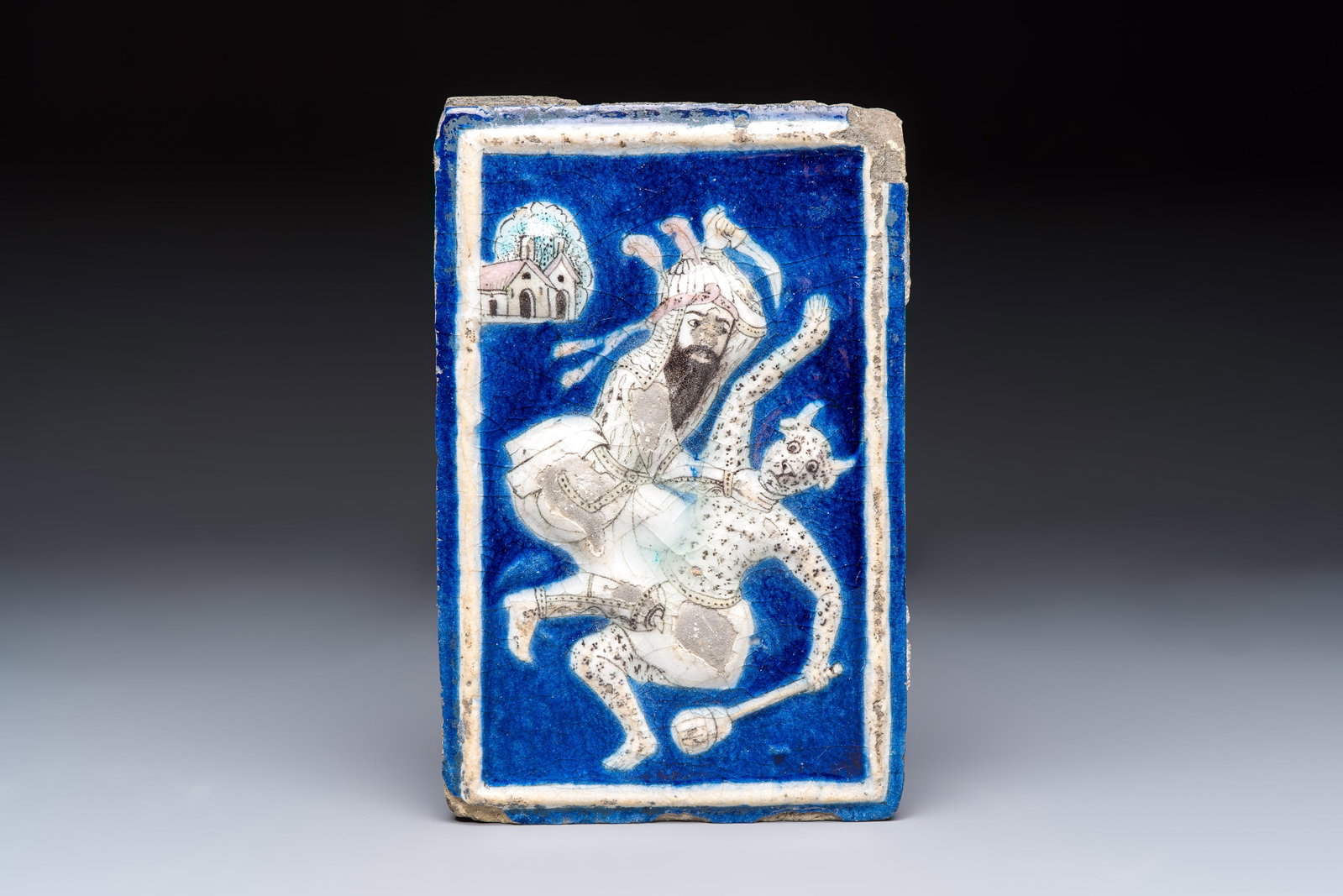 A Persian relief-moulded blue-ground tile depicting Fateh 'Ali Shah in the guise of Rustam slaying: A Persian relief-moulded blue-ground tile depicting Fateh 'Ali Shah in the guise of Rustam slaying the White Div, Qajar, 19th C. Dim.: 26 x 17 x 2,5 cm