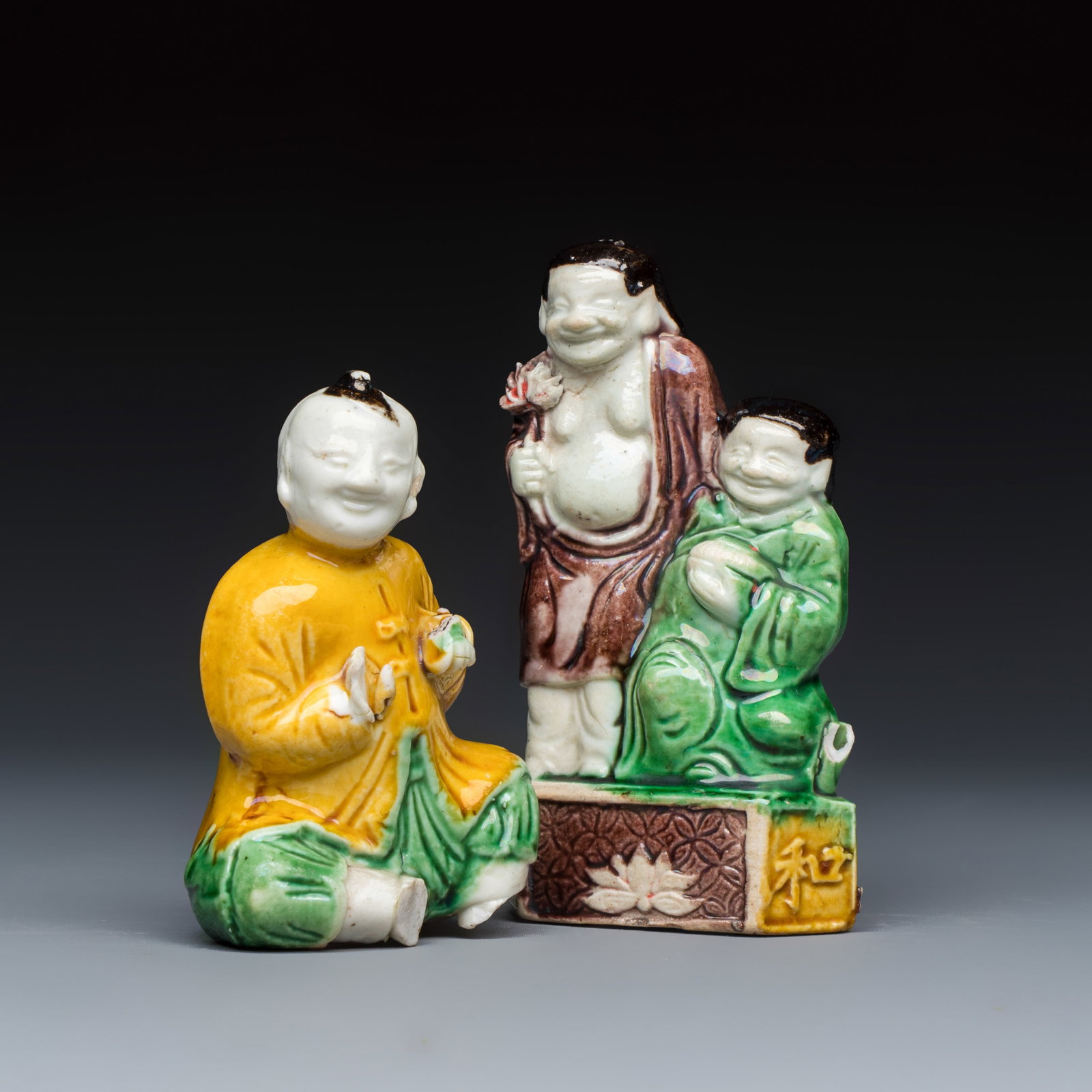 A Chinese famille verte sancai biscuit model of a seated boy and a 'He He Er Xian' group, Kangxi: A Chinese famille verte sancai biscuit model of a seated boy and a 'He He Er Xian' group, Kangxi Dim: 5,5 x 2,6 x 9,8 cm | the group Dim: 5,3 x 3,8 x 7,8 cm | the seated boy