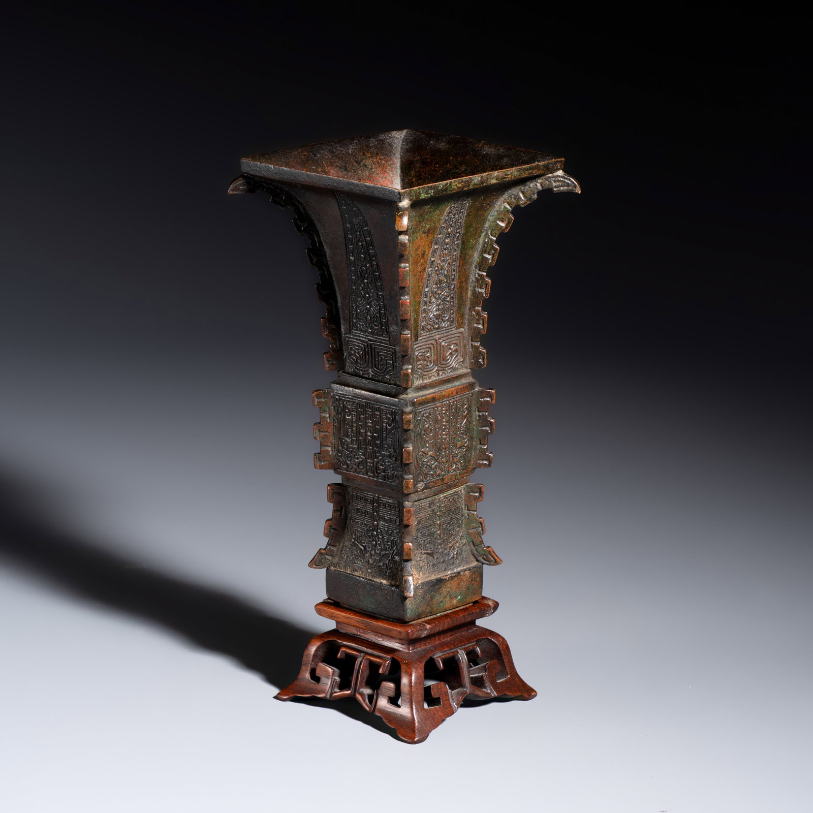 A Chinese bronze archaistic fang zun on a later wooden stand, Ming: A Chinese bronze archaistic fang zun on a later wooden stand, Ming H.: 19,8 cm | incl. stand H.: 16 cm | excl. stand Weight: 500 grams, excl. stand
