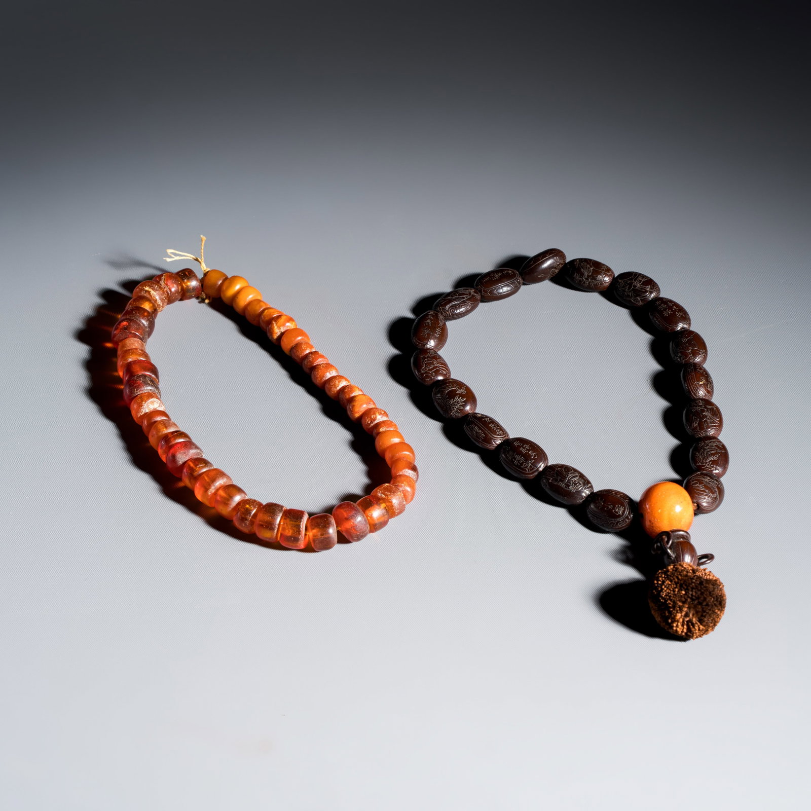 A Chinese carved seed prayer beads and amber beads, 19/20th C.: A Chinese carved seed prayer beads and amber beads, 19/20th C. L.: 34,5 cm | Circumference of the strings Weight:- 22,03 grams, the string with amber beads - 12,38 grams, the string with seed beads