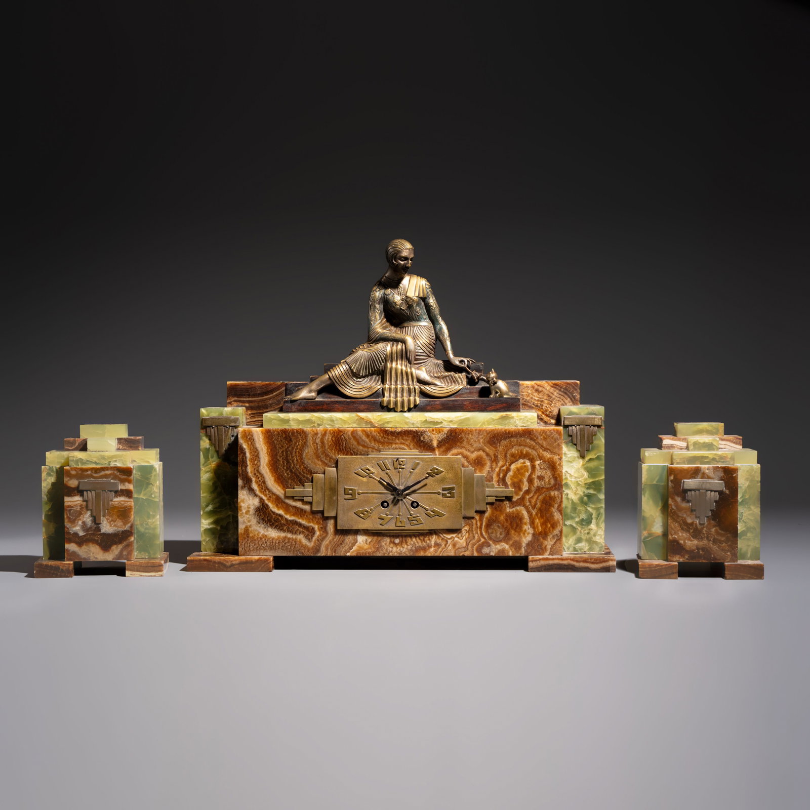 Georges Lavroff (1895–1991): A three-piece Art Deco copper-alloy-mounted green and brown onyx: Georges Lavroff (1895–1991): A three-piece Art Deco copper-alloy-mounted green and brown onyx mantelpiece garniture, 1st half 20th C. Dim: 54 x 13,6 x 42 cm | the mantel clock Dim: 14,8 x 8,2 x 18,7