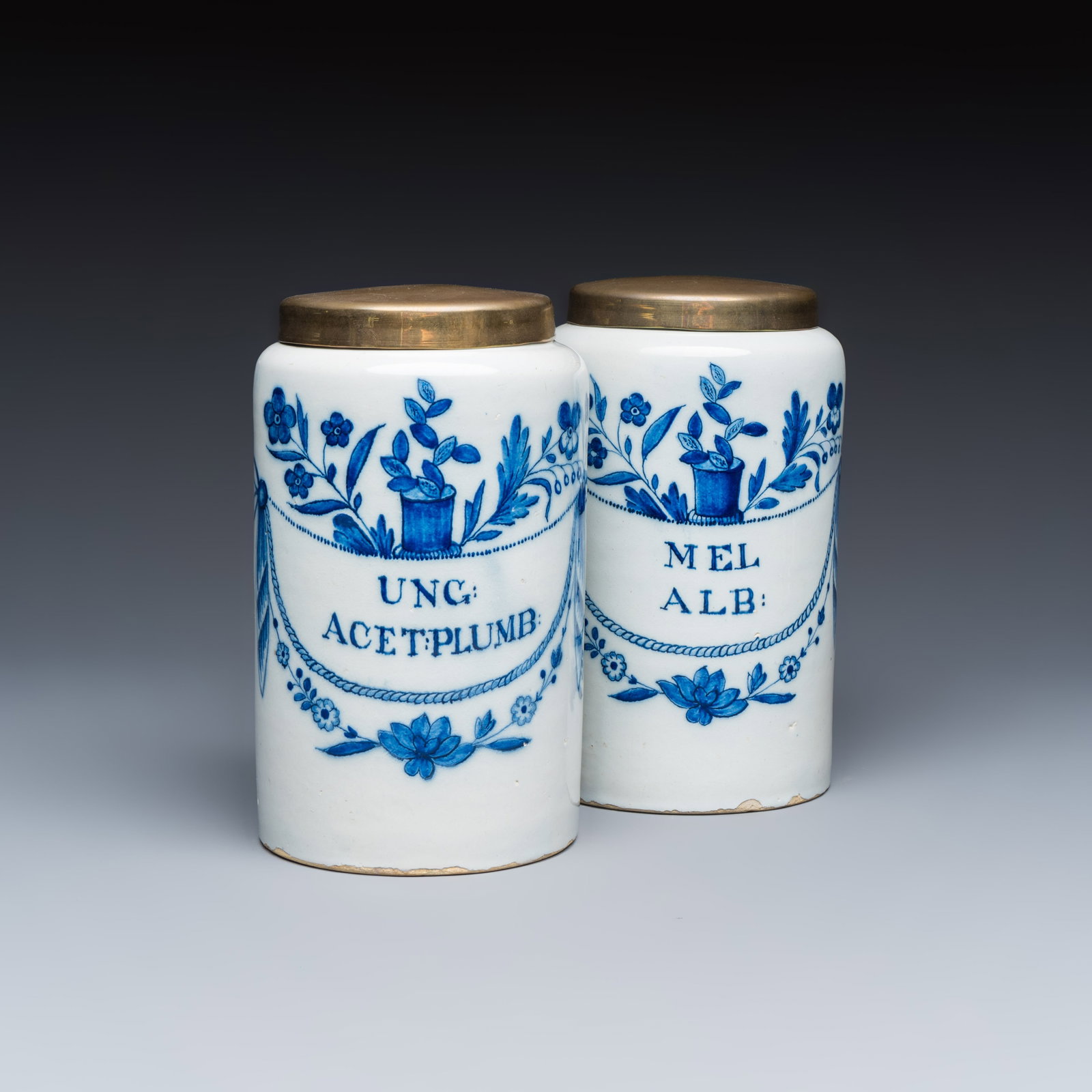 A pair of blue and white Dutch Delft albarelli-type apothecary jars, 18/19th C.: A pair of blue and white Dutch Delft albarelli-type apothecary jars, 18/19th C. H.: 20,2 cm | incl. cover Provenance: A Dutch private collection. Inscribed 'Unc: Acet: Plumb' and 'Mel Alb'. Both marke