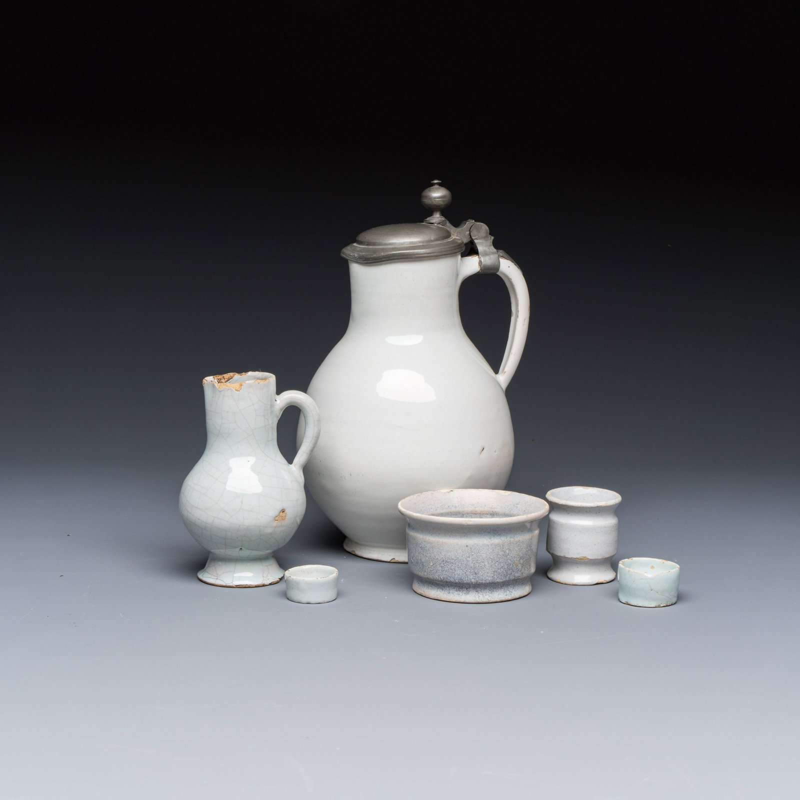 A varied group of six white-glazed Delftwares, 17/18th C.: A varied group of six white-glazed Delftwares, 17/18th C. L.: 14,6 cm - H.: 23,2 cm | the largest jug, incl. mount Dia.: 3 cm - H.: 1,5 cm | the smallest ointment jar