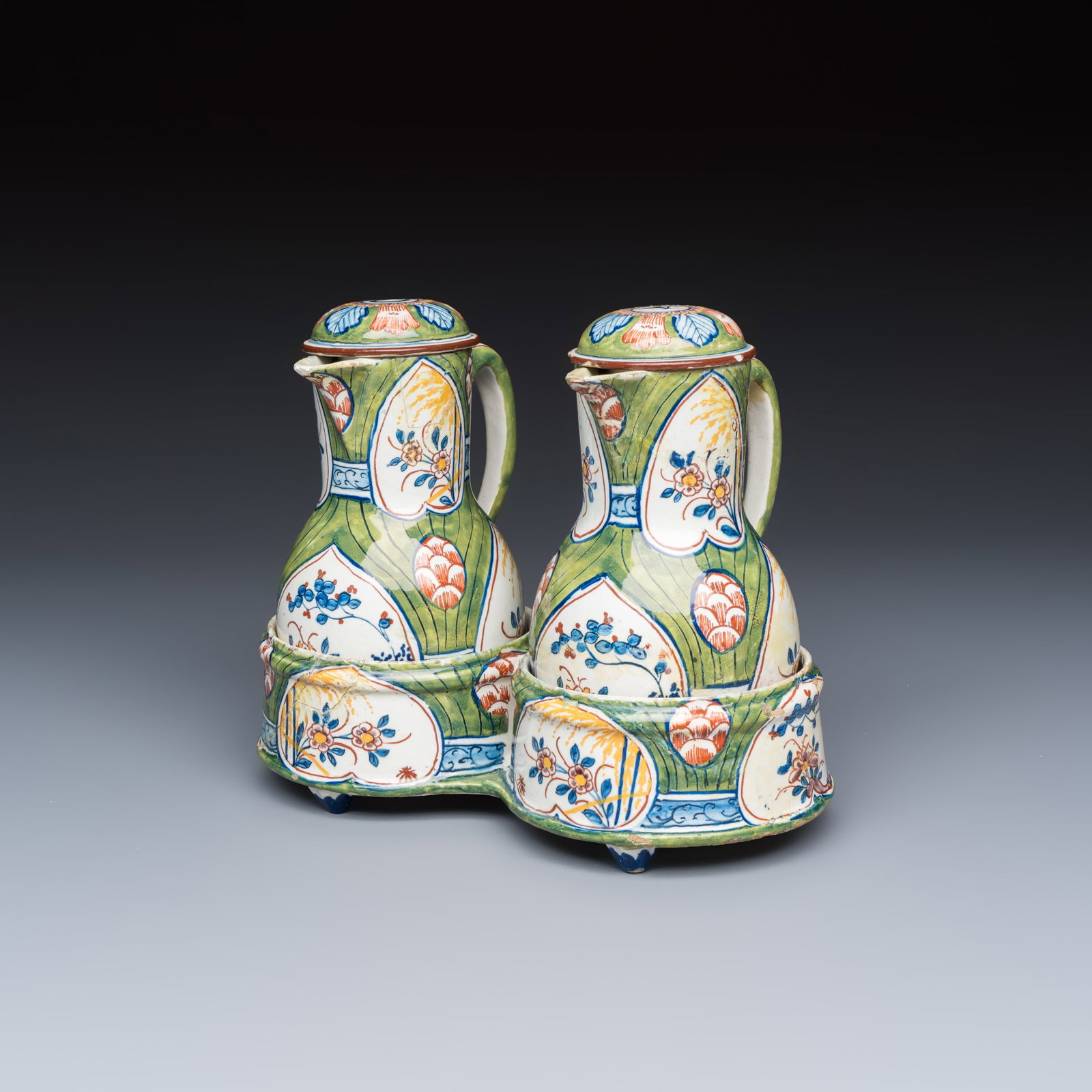 A polychrome Dutch Delft 'Four hearts' oil and vinegar set, 18th C.: A polychrome Dutch Delft 'Four hearts' oil and vinegar set, 18th C. L.: 11,7 cm - H.: 15,1 cm | the oil and vinegar jugs, incl. cover Dim: 20,5 x 11,4 x 5,7 cm | the cruet holder The cruet stand and e