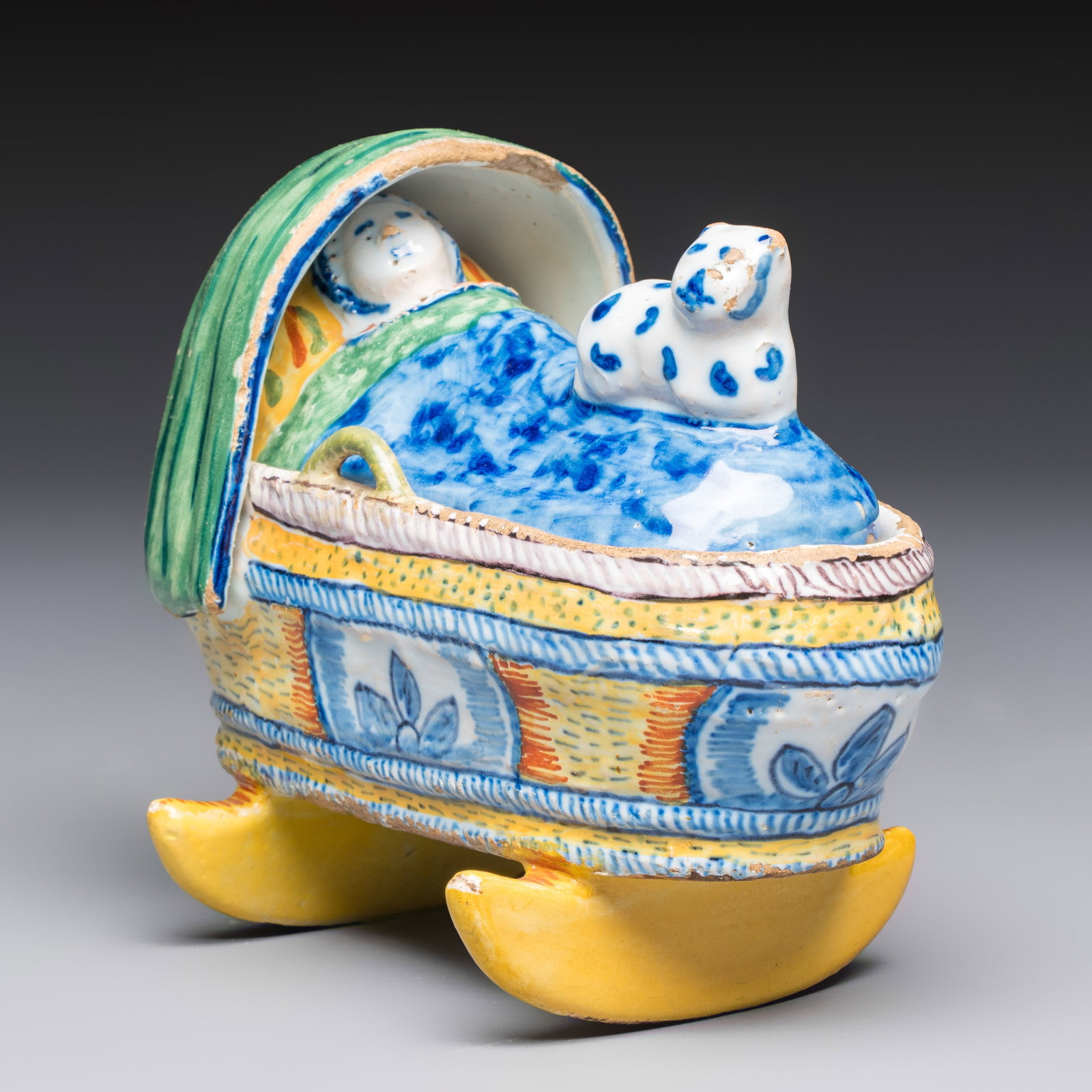 A polychrome Dutch Delft model of a child in a cradle with a cat, 19th C. (1 of 8)