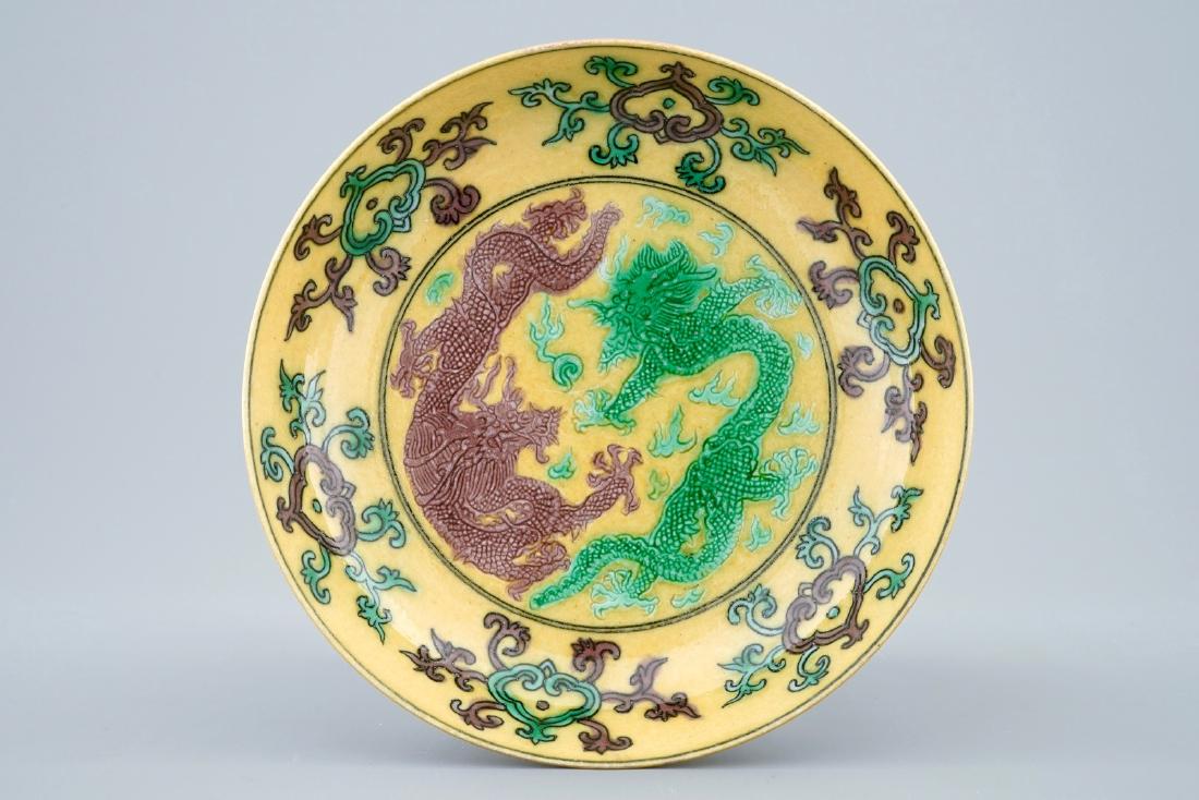 A Chinese yellow-ground saucer with incised green and: A Chinese yellow-ground saucer with incised green and aubergine dragons, Kangxi mark, 19/20th C. Dia.: 13,5 cm