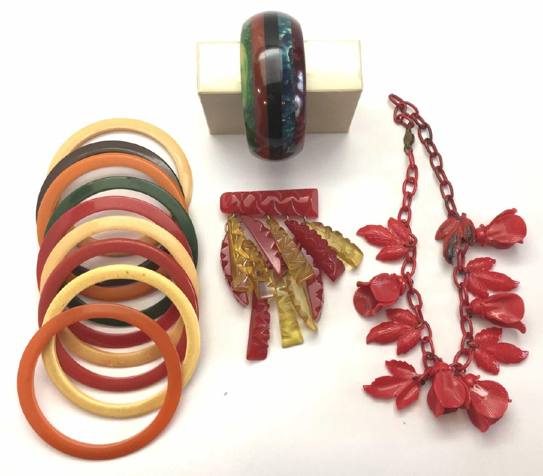 Lot of Vintage Carved Bakelite and Early Plastic: A wonderful Art Deco style lot including a carved red Bakelite dangle pin, a striped "specimen" bracelet, a set of 9 multi-hued bangles and a red celluloid floral necklace. The carved pin measures 2"