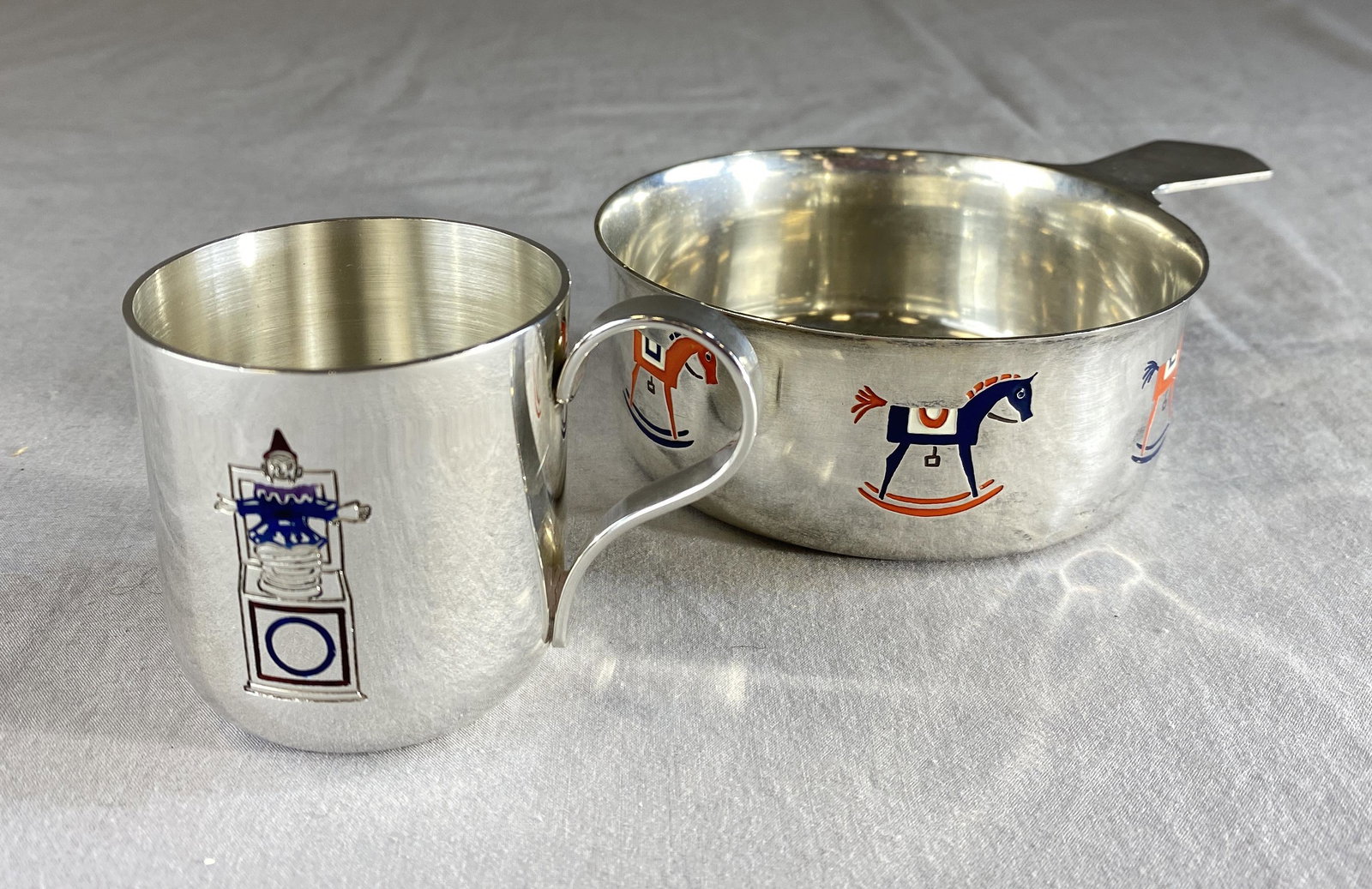 Tiffany Sterling "Toys" Child's Bowl and Cup: From Tiffany and Co., a sterling silver Baby's porringer bowl with enameled rocking horses and a sterling cup with an enameled jack-in-the-box. Both are marked as shown. The bowl measures 4 1/4" in di