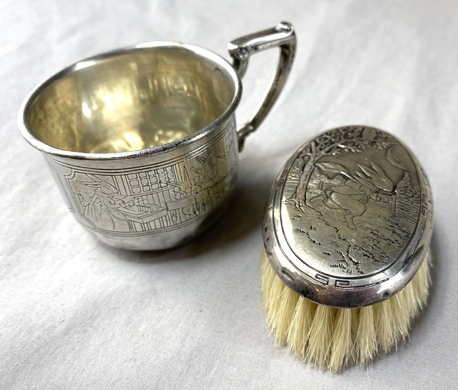 Webster Sterling Peter Rabbit Baby Cup and Brush: From the Webster Co., a sterling silver baby cup and brush in a Peter Rabbitt / bunny pattern. The cup measures 2 1/4" tall and weighs 44 grams. The brush measures 3 " long and weighs 33 grams.