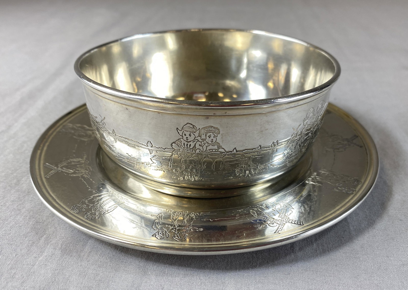 Gorham Sterling Baby Bowl with Under Plate: A sterling silver nursery set from Gorham in a Dutch children pattern. It includes a 6 3/8" plate weighing 105 grams and a 4 3/8" diameter bowl weighing 131 grams.
