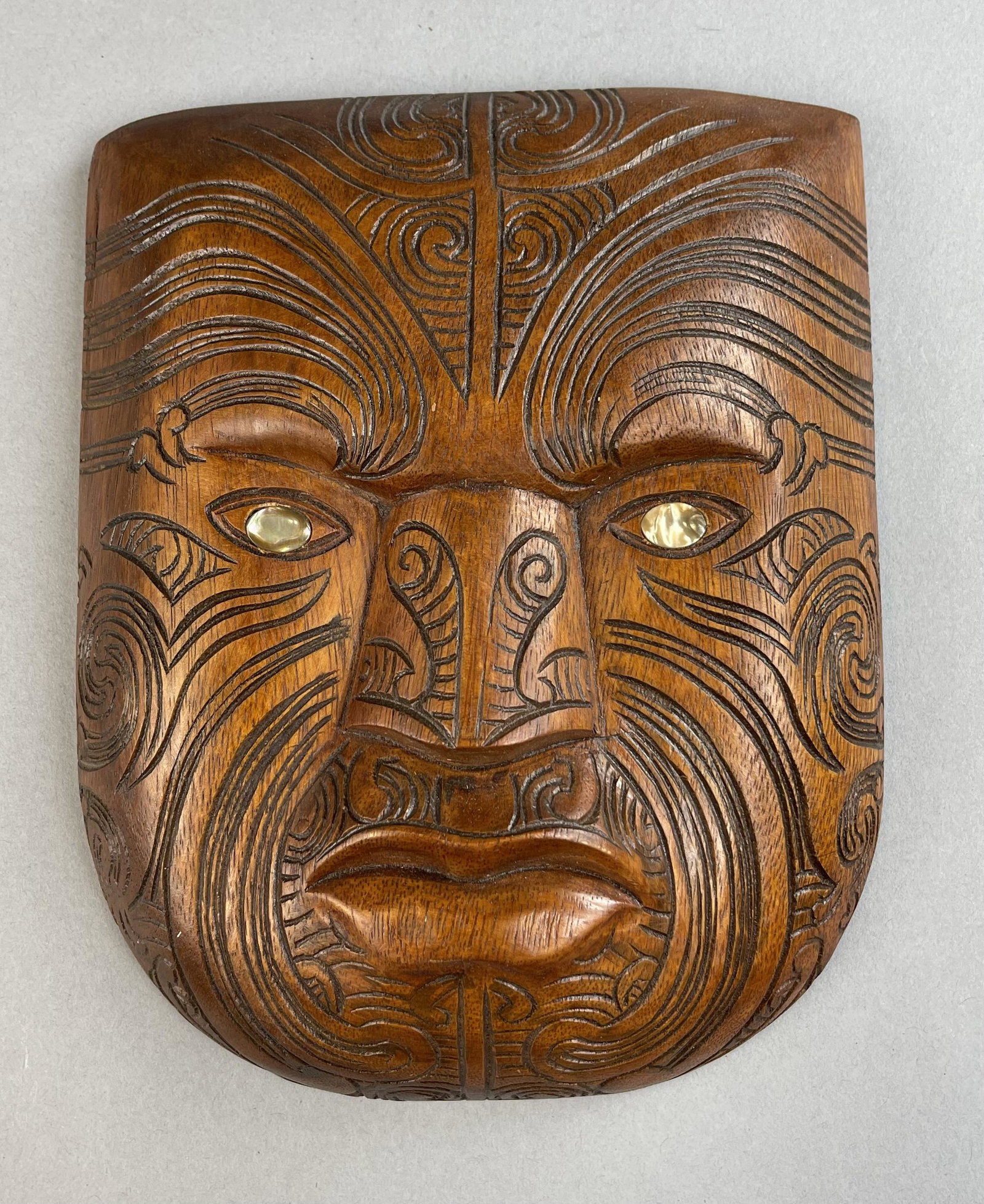 Maori Tatoo Carved Wooden Mask New Zealand: Carved wooden mask with mother of pearl eyes. 7-1/2" x 9-1/2" Shipping: In-House shipping available for this lot. Please read the shipping section in our full Terms and Conditions for all information 