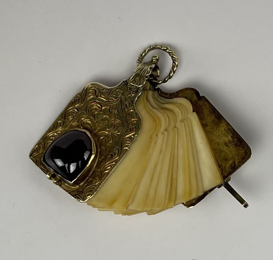 19th Century. Gold Note Pad Book Pendant: Chased unmarked yellow gold toned metal cover with a cabochon garnet circa late 19th early 20th century. Pages appear to be bone or celluloid. SHIPPING: In-House Shipping Available for this lot. Pleas
