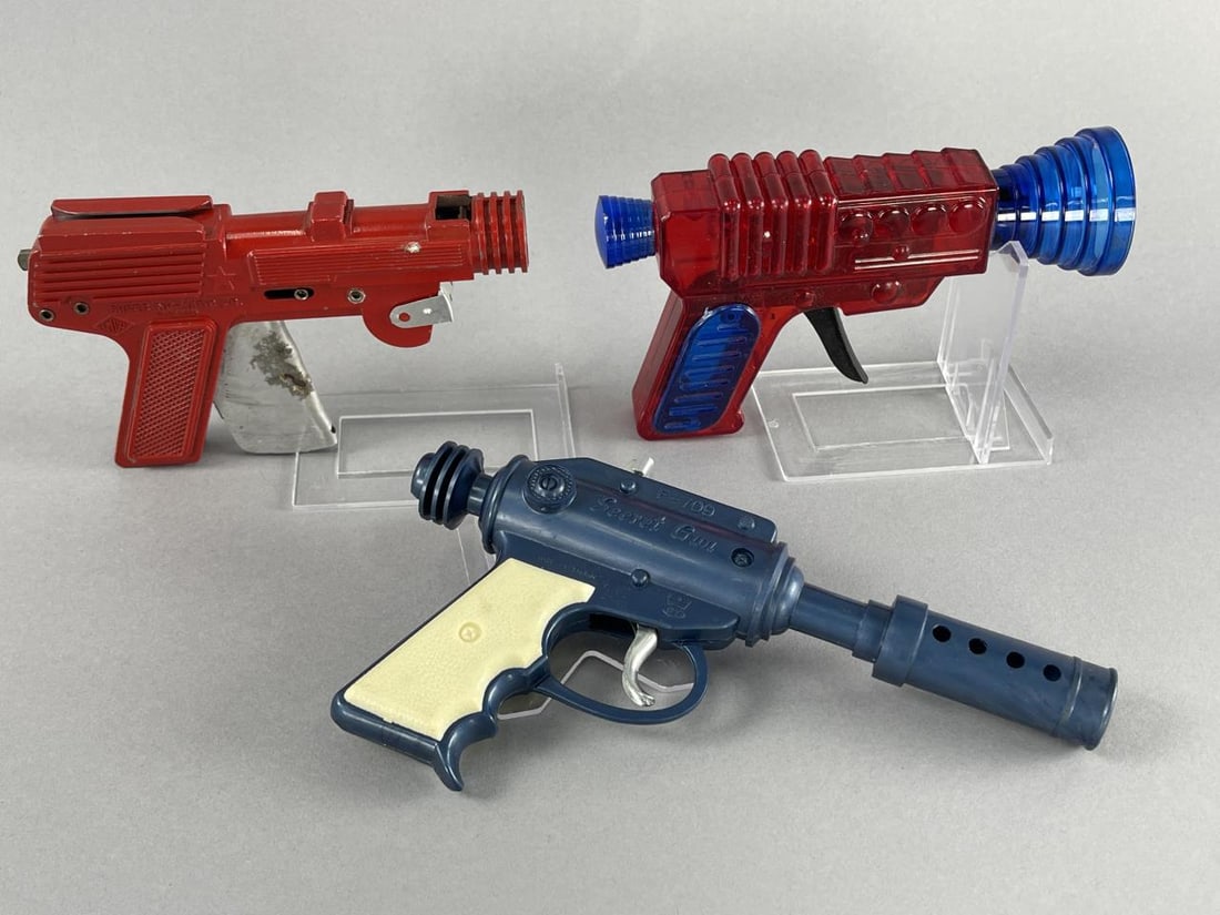 LMCO Nu-Matic Jr., Secret Gun F-709, Red Space Gun: 5.75'' x 3.5'' LMCO Super Nu-Matic Jr. metal cap gun.6.25'' x 3.75'' red and blue plastic friction toy, believe it is ceased.Secret Gun F-709 DY Made in Taiwan, plastic cap gun, 7.75'' x 4.5''.