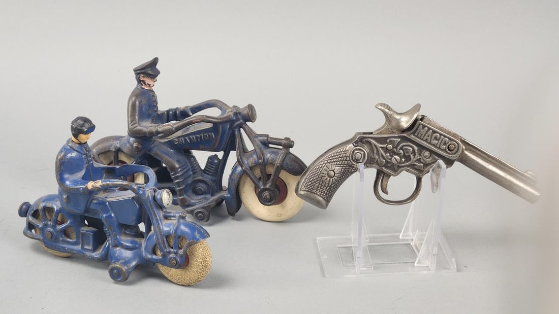 2 Cast Iron Police Motorcycles & Magic Toy Cap Gun: Circa 1930s 7'' blue Champion Twin V cast iron Police motorcycle.Vintage 6'' cast iron Police motorcycle, head has been replaced.Appx. 6'' cast iron Magic toy cap gun.