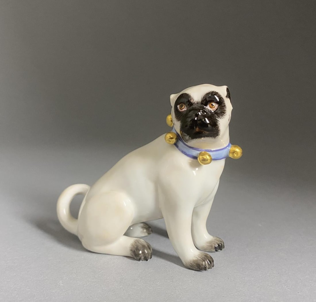 Meissen Porcelain Figure of a Seated Pug Dog 3": Meissen porcelain figure of a seated pug dog wearing a blue collar with gold painted bells, marked on underside with the underglaze blue crossed swords mark, and painted "77", 2-7/8" H.