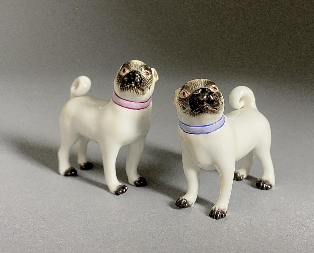2 Miniature Meissen Porcelain Figures of Pug Dogs: Two miniature Meissen porcelain figures of pug dogs, one wearing a pink colored collar and the other one wearing a light blue collar, marked on underside with the underglaze blue crossed swords mark, 