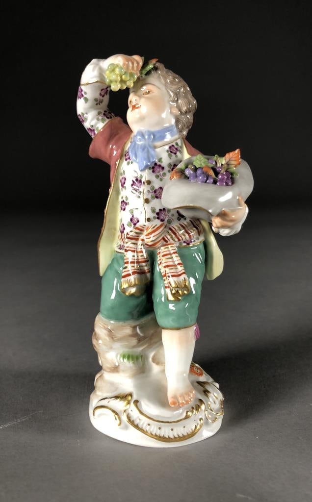 Meissen Porcelain Figurine Boy Holding Grapes F 21: Hand painted Meissen porcelain figurine of a boy holding grapes, first modelled by Michel Victor Acier (French, 1736 - 1799), blue crossed swords mark on bottom as well as incised "F 21", approximatel