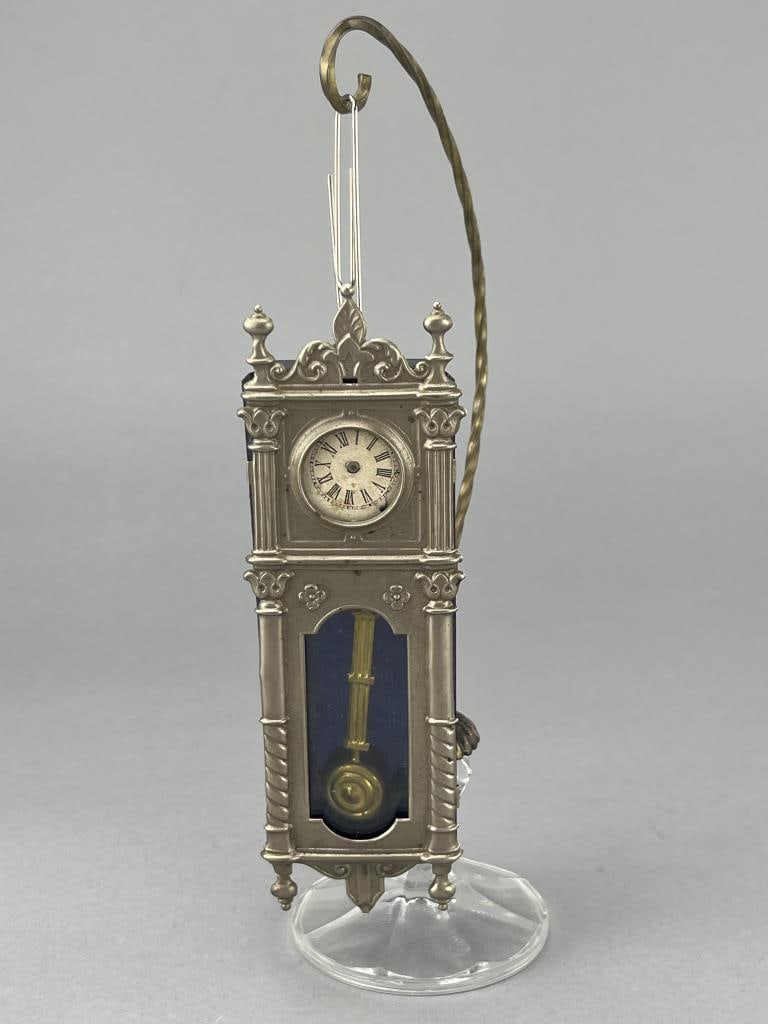 Metal Wind Up Wall Clock 5 3/4 X 1 3/4": Front is soft metal, back is tin. Opens to wond up. Does not work. One hand missing. Front sides off. Maker unknown. Stand for clock not included.