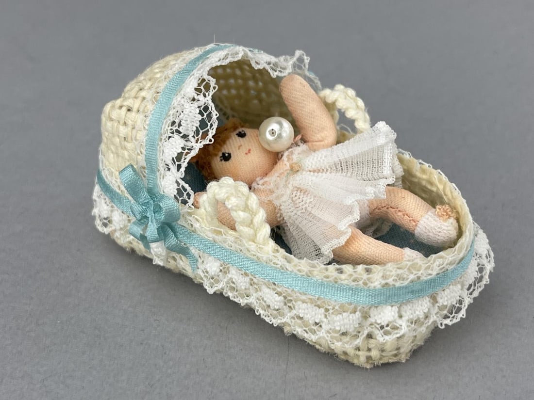 Wee Folks Handmade Baby W/Wicker Basket: This tiny 2" doll is entirely hand stitched with painted face and lace clothes. 2 pink bows and pink rattle and 2 pink bows on her socks, Basket is 3 3/4 x 1 1/2" with blue trim and polka dot fabric.