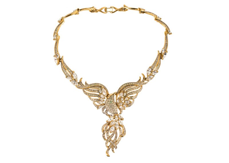 A Trifari goldtone necklace in the shape of a bird with: A Trifari goldtone necklace in the shape of a bird with spread wings, set with rhinestones. Signed Trifari. L. 41 cm.