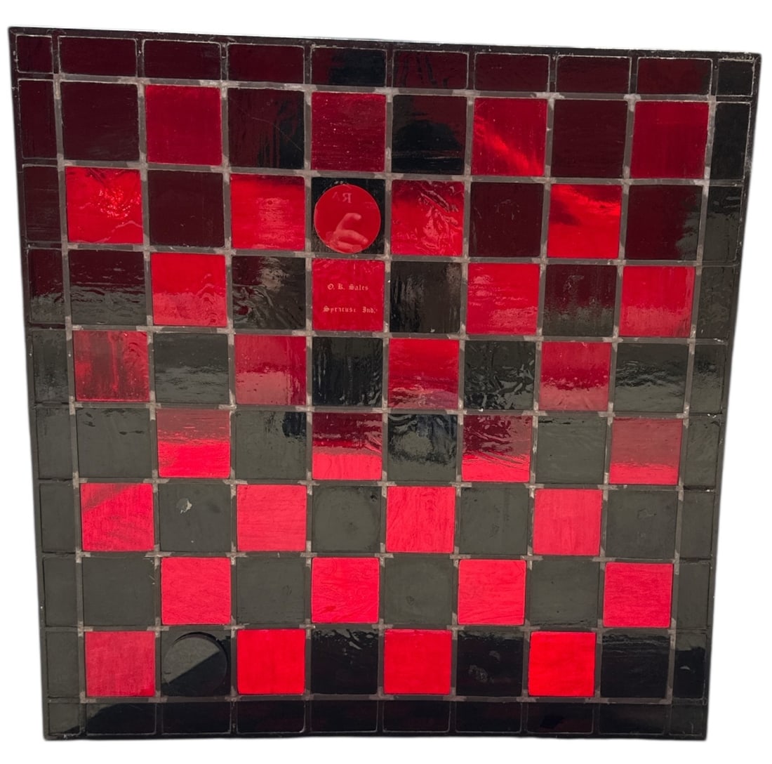 A Folk Art Advertising Stained Glass Window: 36" H x 36" W x .25" D. Checkerboard pattern with a solid black border. Two of the red stained glass pieces are marked. One says "O.K. Sales Syracuse, IND". The other pieces says "Kip Sullivan Leesbur
