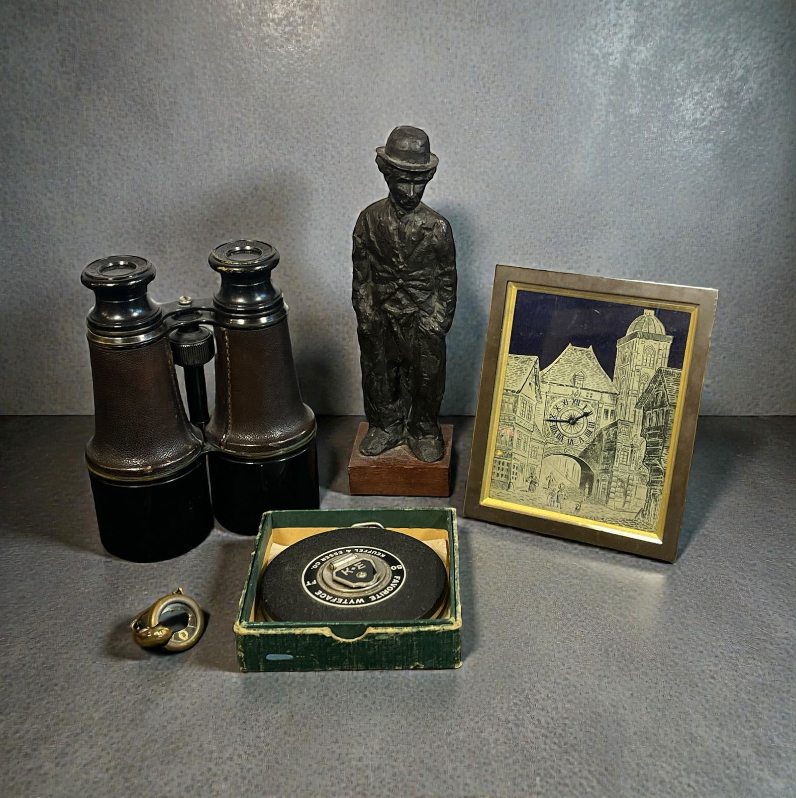 Global Gentleman's Articles: Includes a set of binoculars, cast metal sculpture of Charlie Chaplin by Guido Messer, compass, a framed clock, and a measuring tape by Keuffel and Esser Co.