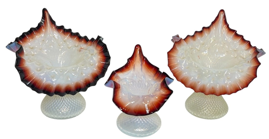 Three Oxblood and Opalescent Art Glass Jack In The Pulpit Vases: Featuring ruffled edged and crosshatched base jack-in-the-pulpit victorian vases. The larger vases measures 7" H x 6.25" W x 4" D, the smaller vase measures 5.5" H x 4.25" W x 3.25" D.